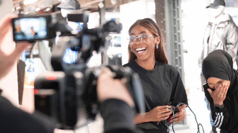 A behind the scenes shot of a video production. Adidas staff taking part in a video. They are both smiling and laughing, looking at the video team.
