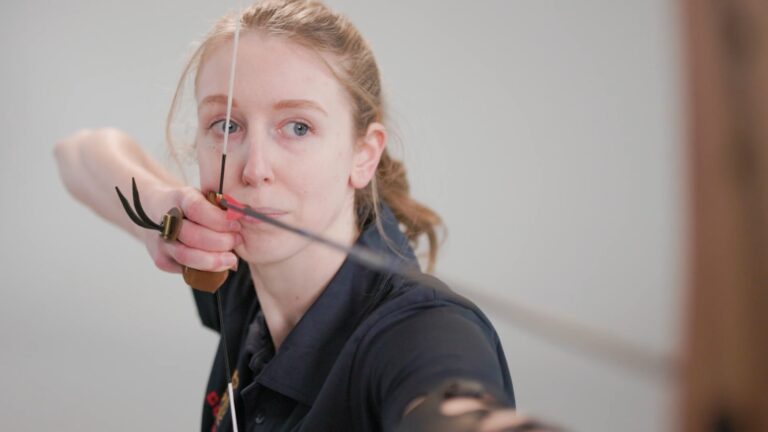 A close up of an archer pulling back the string on her bow with an arrow ready to shoot.